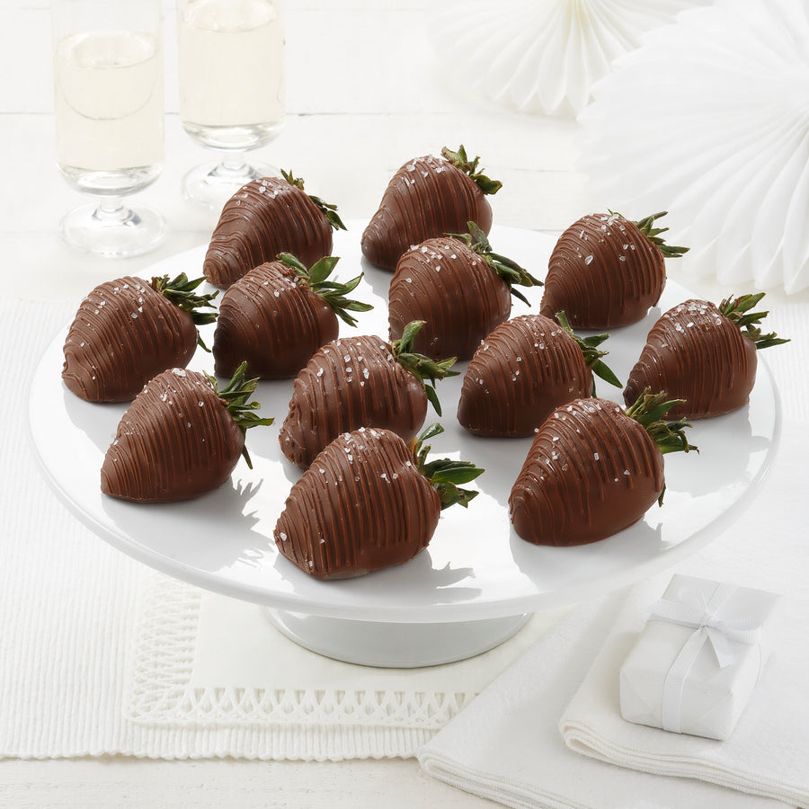 A plate of chocolate-covered strawberries with sea salt on top, presented on a white plate with a white background.