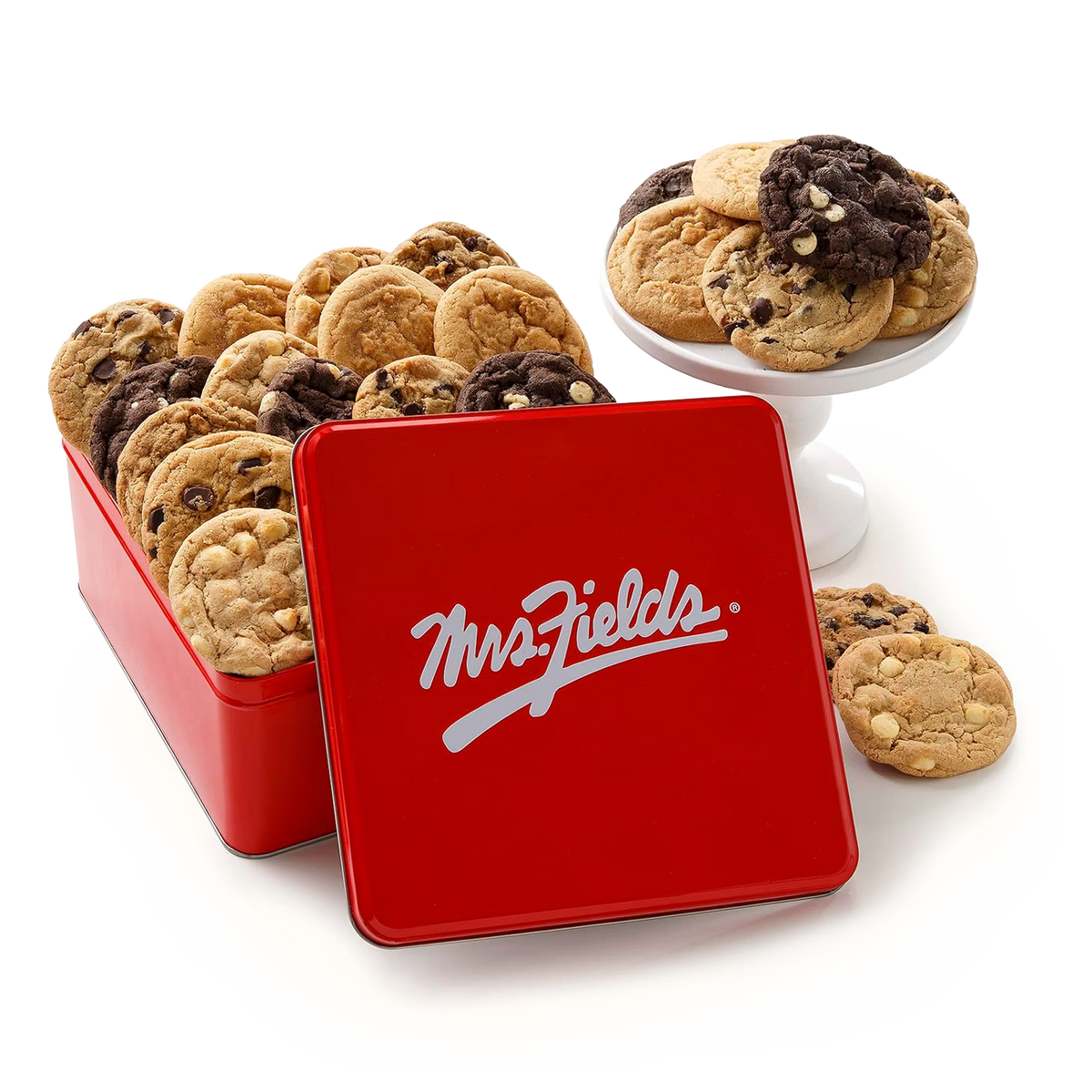 A red metal cookie tin with the brand name 'MrsFields' in white script on the lid, shown open with assorted chocolate chip cookies inside. A white pedestal stand holds additional cookies, and a few cookies are placed on the white surface around the tin.