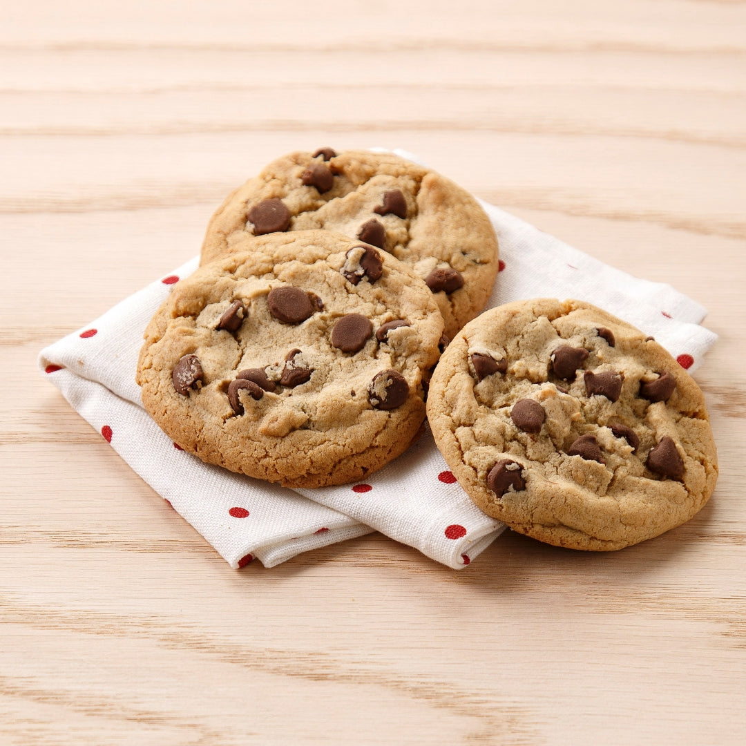 Three chocolate chip cookies on a white napkin with red polka dots, set on a light wood surface.