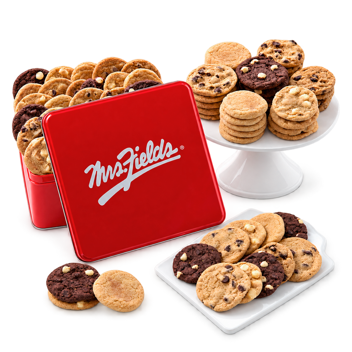 A red metal cookie tin with the white Mrs. Fields logo, shown open with assorted cookies inside and additional cookies displayed on white stands and plates against a clean white background.