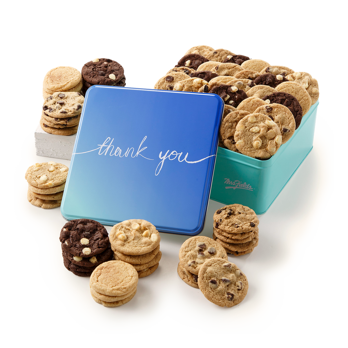A blue gradient square tin with 'thank you' in white script, filled with assorted cookies and surrounded by chocolate chip and cookie stacks on a white background. The side of the tin shows the Mrs Fields logo.