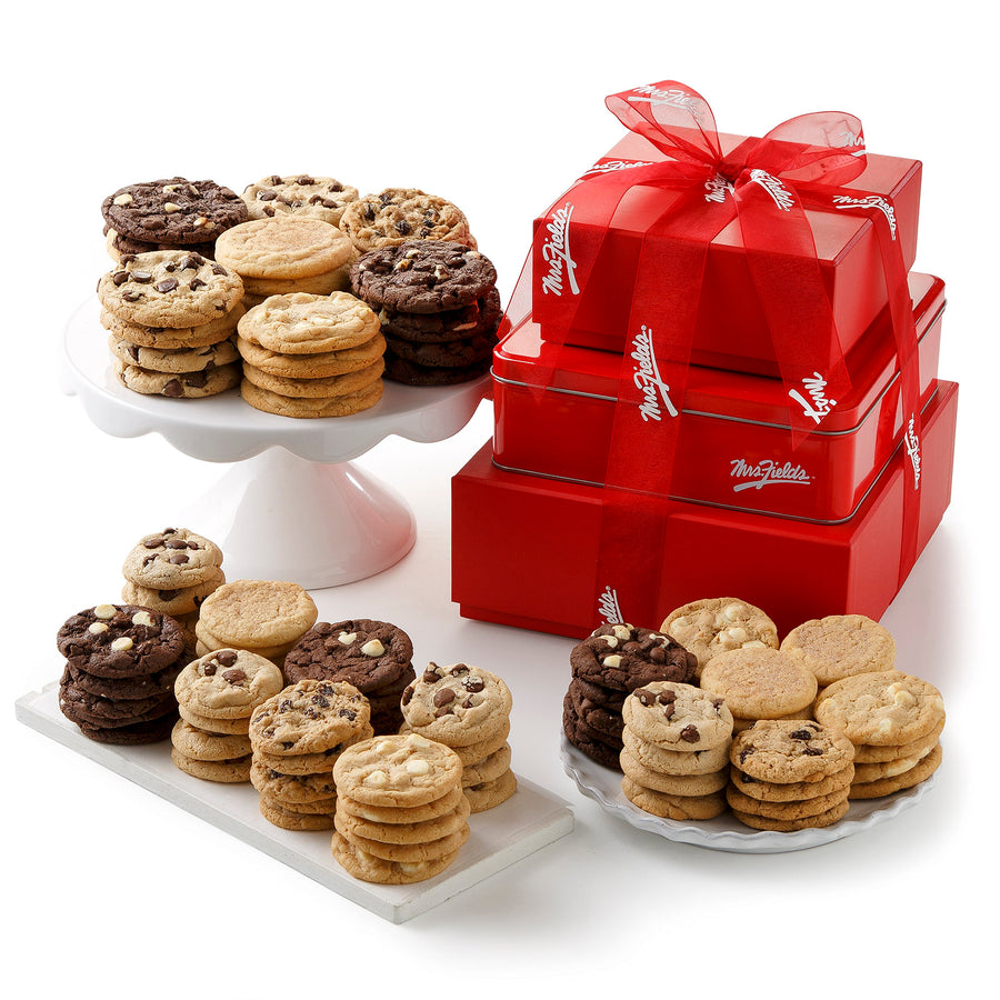 A three-tiered red tower tied with a red Mrs. Fields ribbon surrounded by a large assortment of both big and small cookies on a blank white surface.