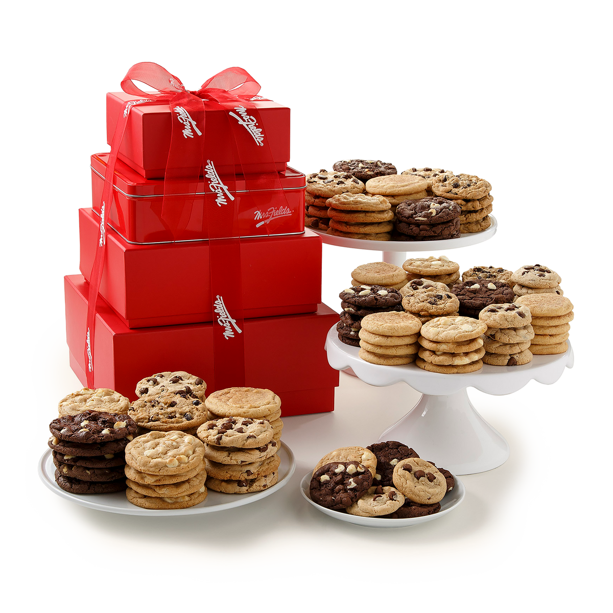 A gift set of red stacked boxes tied with white ribbons, displayed alongside assorted cookies on white plates and cake stands against a clean white background.