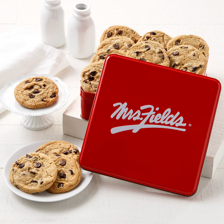 Mrs. Fields signature red cookie tin with a dozen semi-sweet chocolate chip cookies on a white surface with plates and milk bottles.