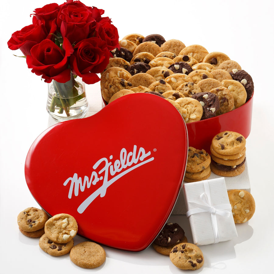 Mrs. Fields signature heart shaped tin filled with an assortment of Nibblers bite-sized cookies on a white surface with red roses