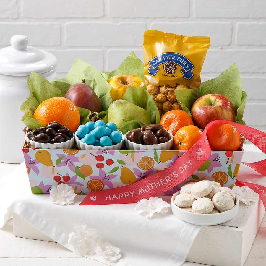 A Mother's Day gift crate filled with fruits, chocolates, treats, and tea cookies on a white surface with a Happy Mother's Day ribbon.