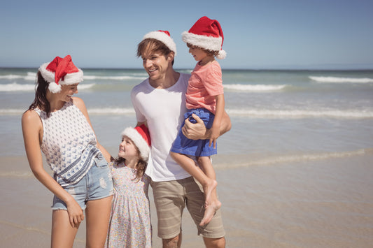 Happy family wearing Santa hats at the beach to celebrate Christmas in July 