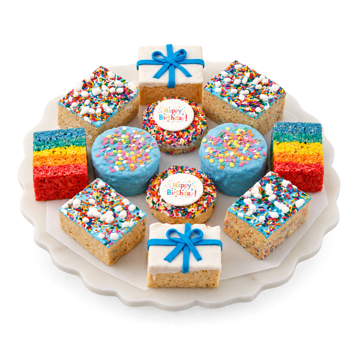 A round white platter holding assorted birthday-themed baked treats: several square rice-cereal bars topped with colorful sprinkles, two round blue-frosted bars with sprinkles and a white 'Happy Birthday' topper, two square bars decorated with white icing and blue bow toppers, and two rainbow-striped bars. The platter is photographed on a clean white background.