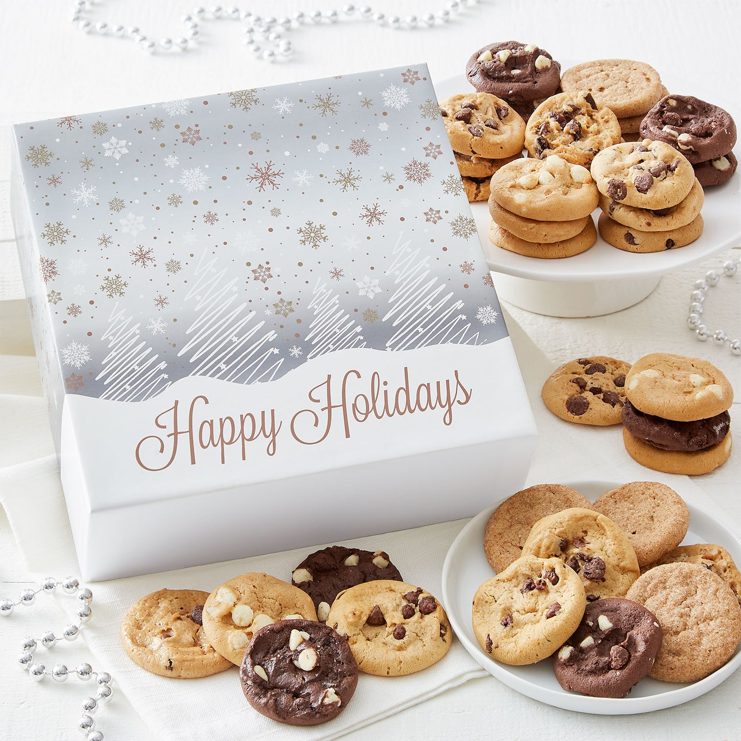 A Happy Holidays gift box decorated with a winter wonderland scene and surrounded by an assortment of Nibblers®