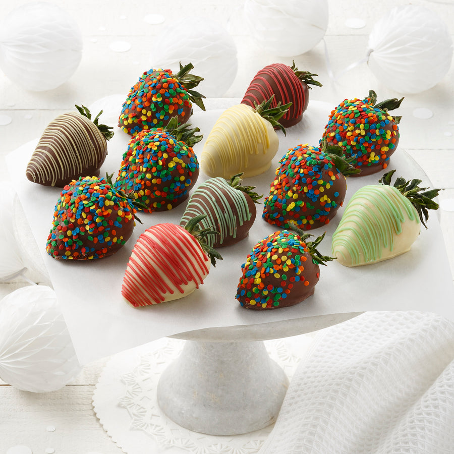 A dozen chocolate covered strawberries, some decorated with colorful red, orange, yellow, blue, and green sprinkles, and some drizzled with different colors of white chocolate.