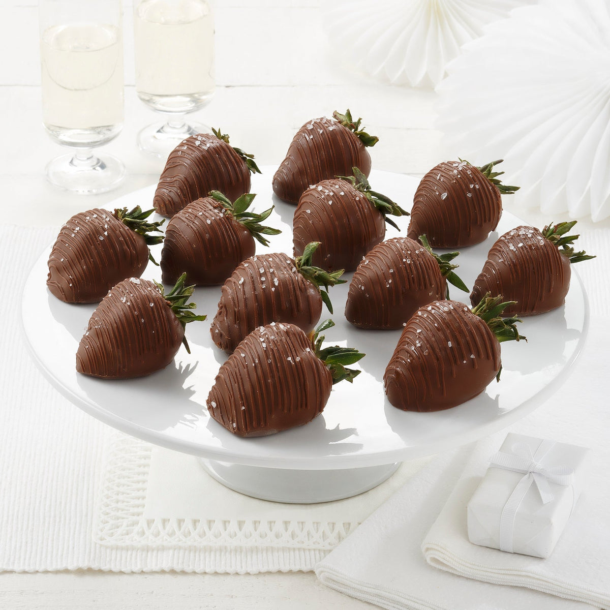 A plate of chocolate-covered strawberries with sea salt on top, presented on a white plate with a white background.
