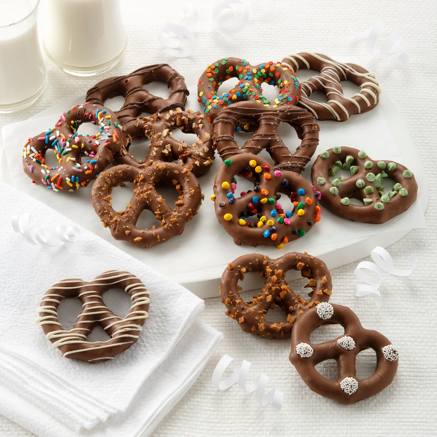 A variety of chocolate-covered pretzels with different toppings, such as sprinkles, candies, and toffee, on a white surface.