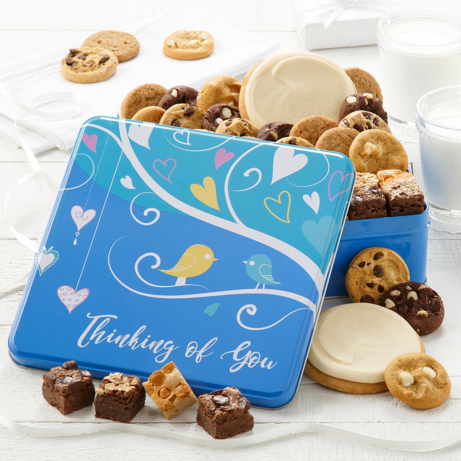 A blue Thinking of You gift tin filled with an assortment of nibblers, brownie bites, and two white frosted round cookies