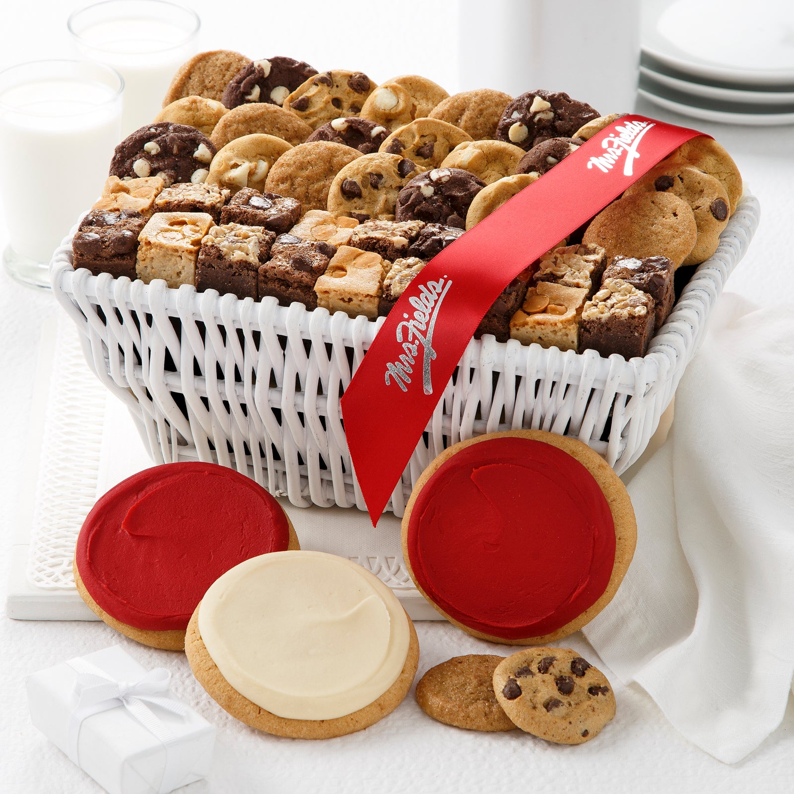 A white gift basket filled with an assortment of nibblers, brownie bites, and red and white frosted round cookies