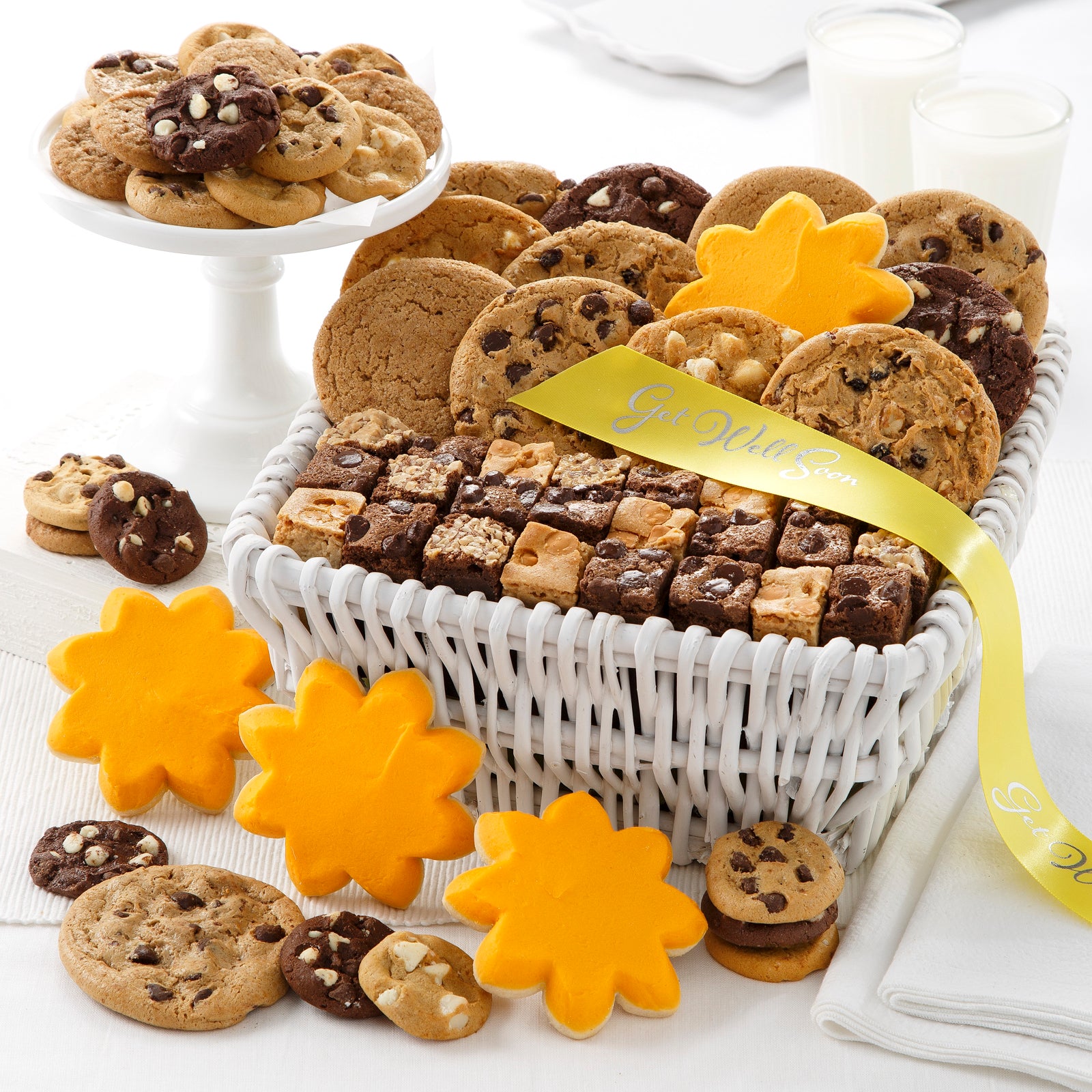 White gift basket filled with an assortment of nibblers, original cookies, brownie bites and frosted sunshine cookies tied with a yellow get well soon ribbon