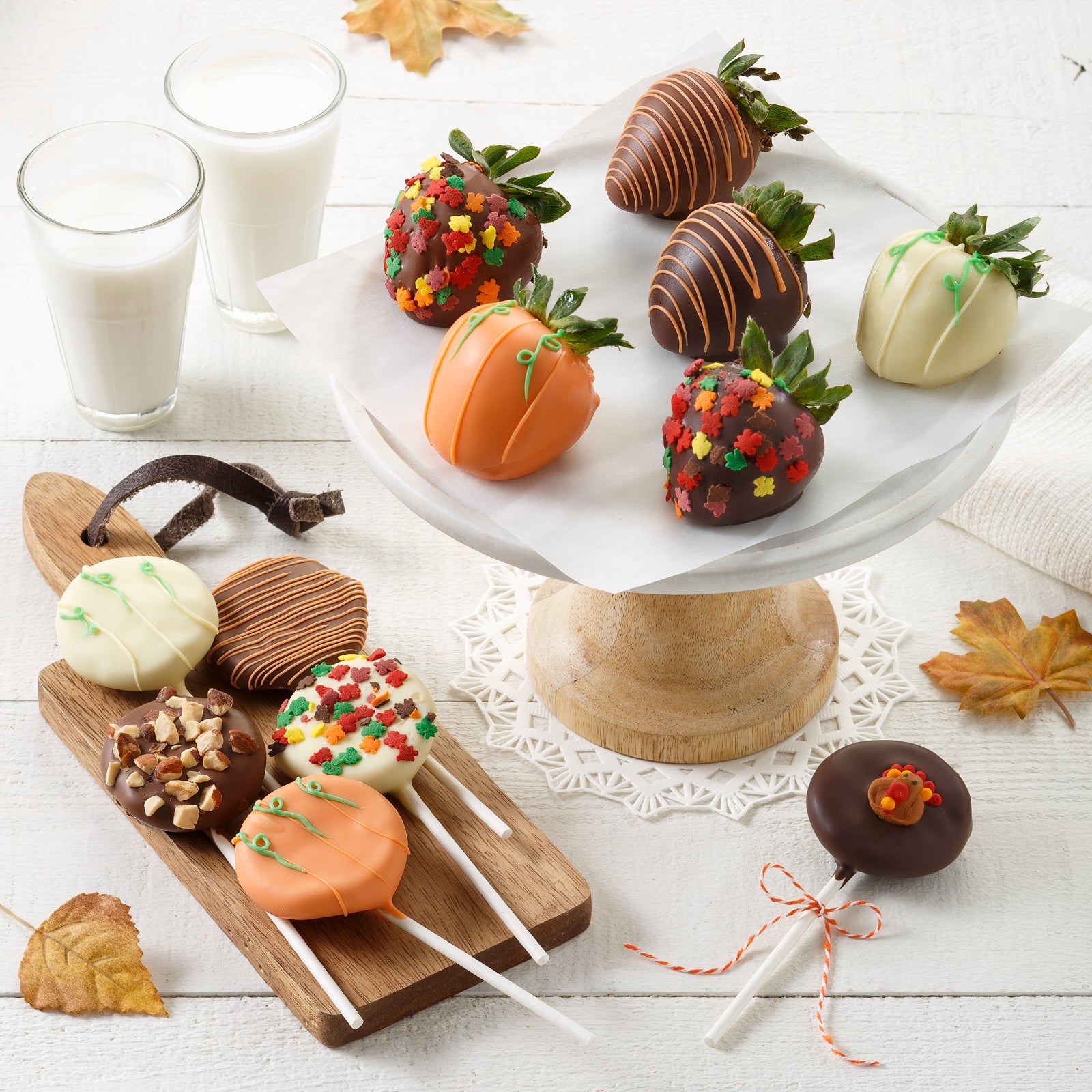 An assortment of chocolate covered strawberries and Nibblers Bite-Sized Cookies on sucker sticks decorated in an autumnal theme and color scheme with fall leaf sprinkles.