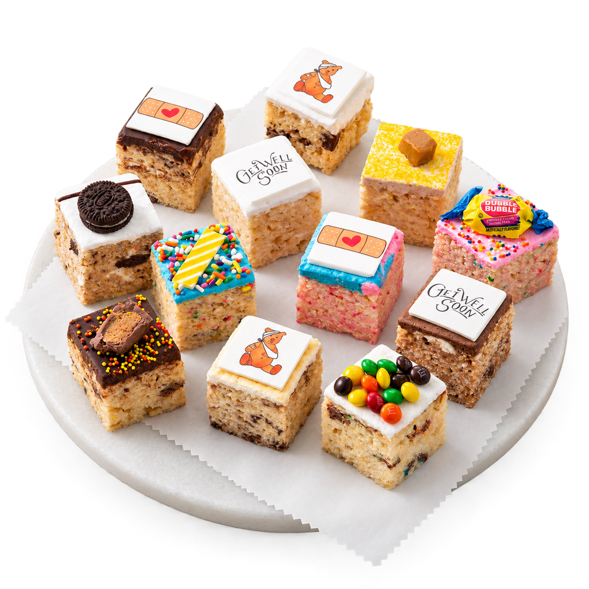 A set of 12 customized baby shower cake toppers arranged on a white plate with a piece of parchment paper, styled with two glasses of milk on a white wooden table.