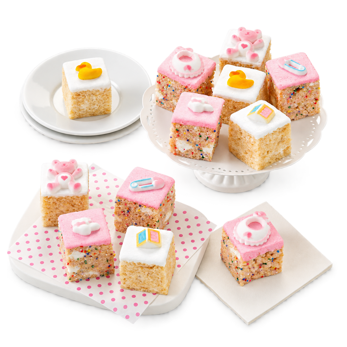 A set of baby-themed rice cake slices decorated with pink, white, and yellow frosting, sprinkles, and cute accents like rubber ducks, hearts, and letters, arranged on white plates and a pedestal.