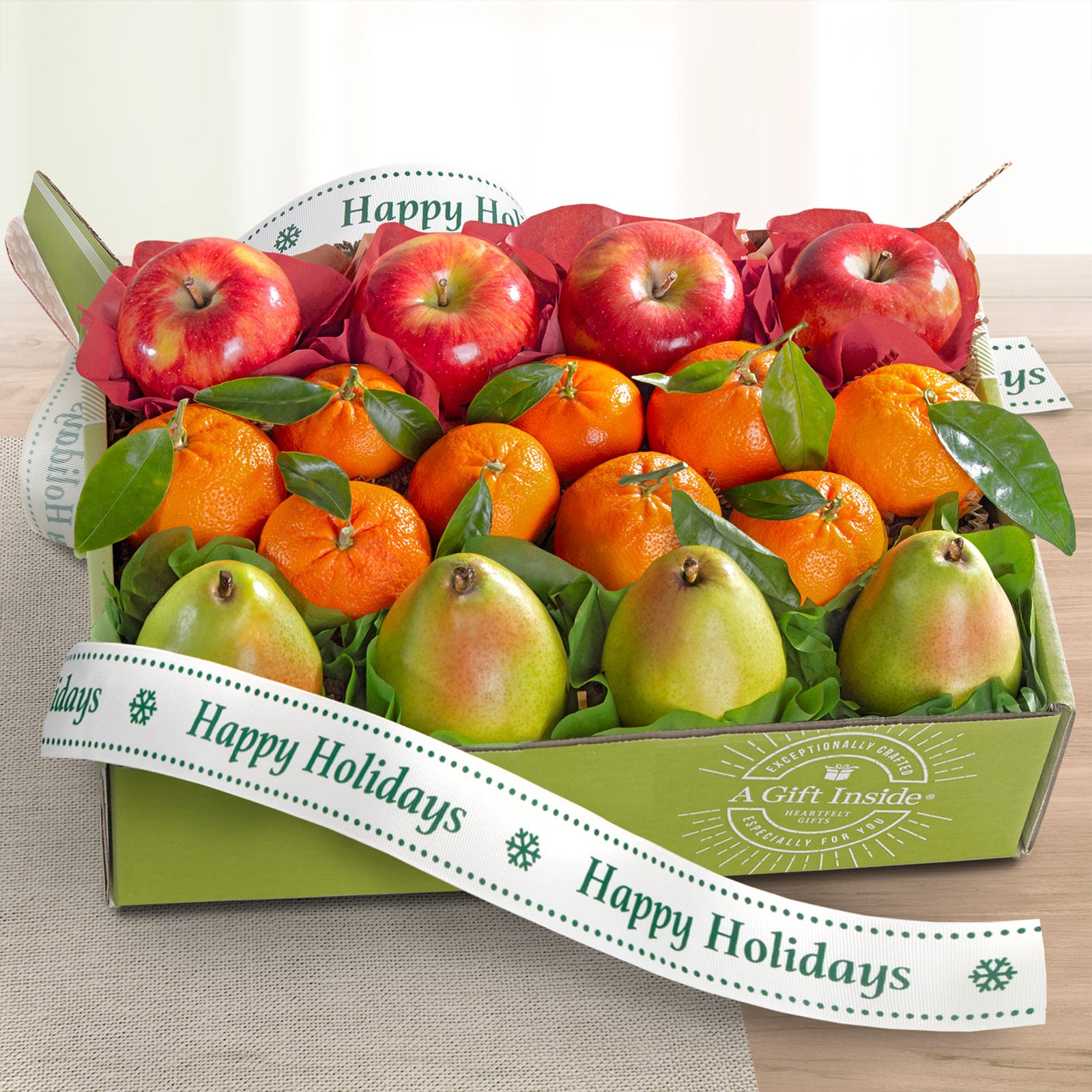 A gift box of fresh fruit including red apples, mandarin oranges, and green pears in a box with a "Happy Holidays" ribbon.