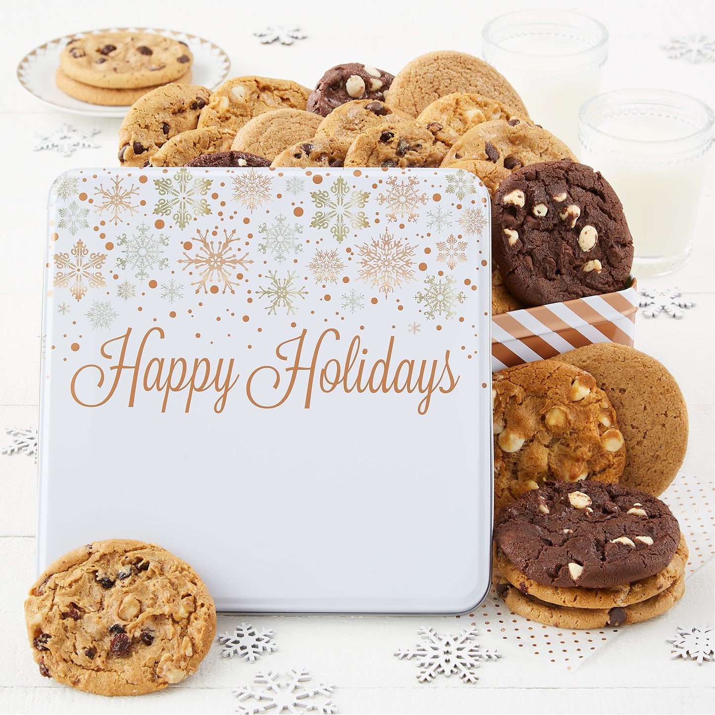 A Happy Holidays gift tin decorated with silver and gold snowflakes on a white top and filled with an assortment of original cookies