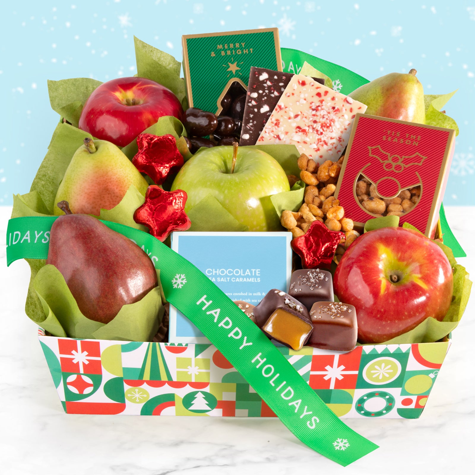 A decorative holiday crate filled with an assortment of fruit, nuts, and chocolate with a green ribbon that says "Happy Holidays"