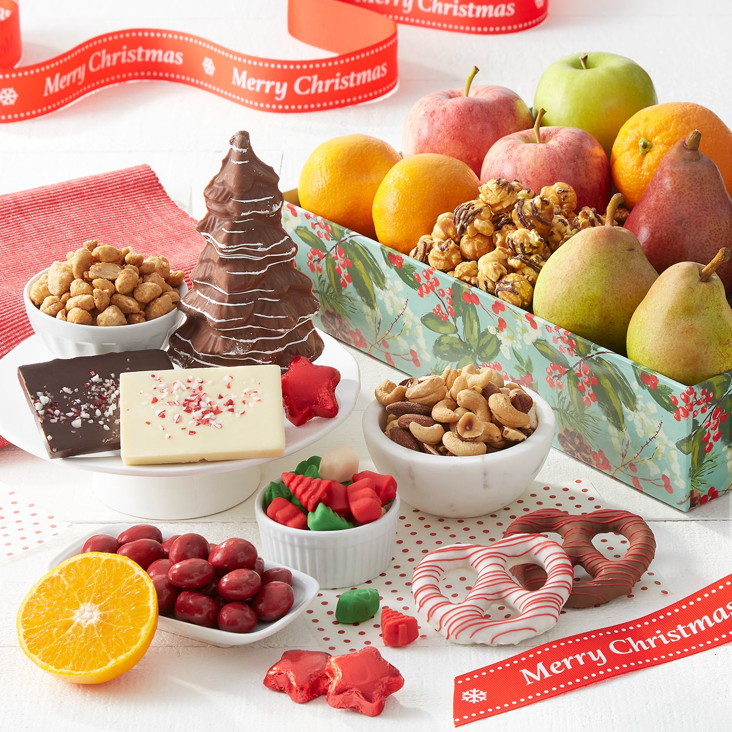 A decorated holiday crate filled with an assortment of fruit, nuts, popcorn, chocolate-covered pretzels, candy, and chocolate.