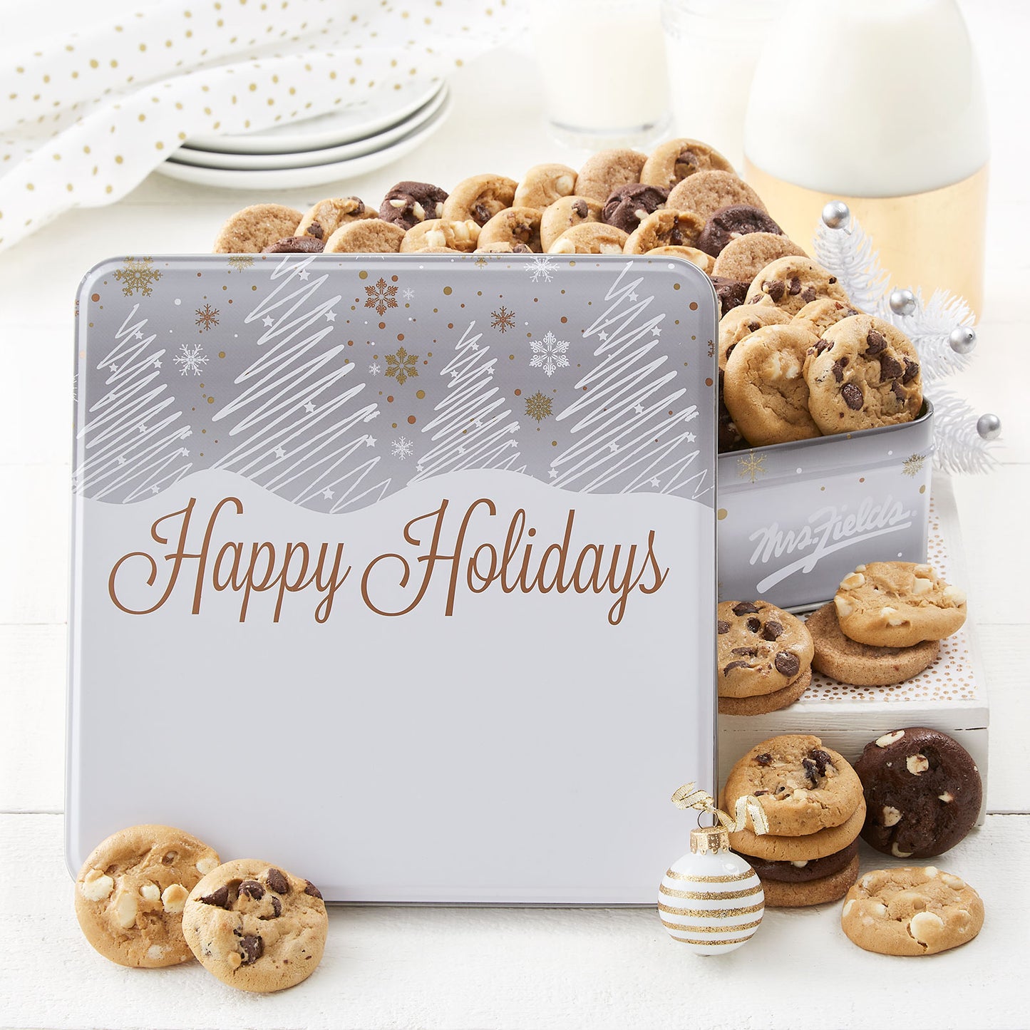 A Happy Holidays gift tin that is decorated with a white, silver, and gold winter scene and filled with an assortment of Nibblers®