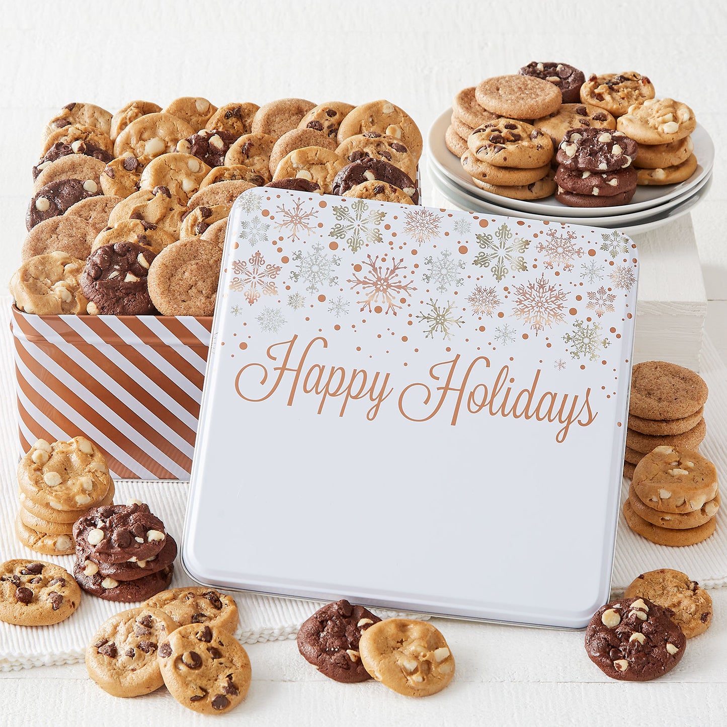 A Happy Holidays gift tin decorated with silver and gold snowflakes on a white top and filled with an assortment of Nibblers®.