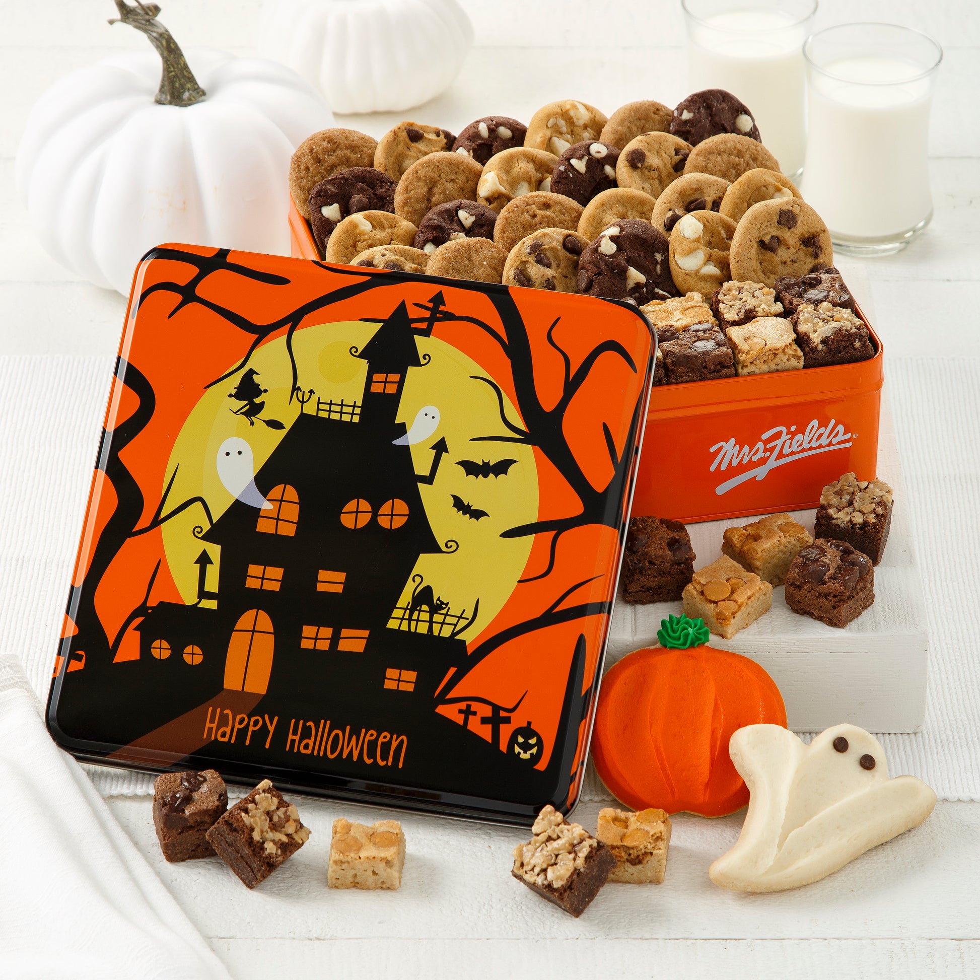 A Happy Halloween gift tin decorated with a spooky haunted house and filled with an assortment of Nibblers®, brownie bites, one frosted pumpkin cookie, and one frosted ghost cookie