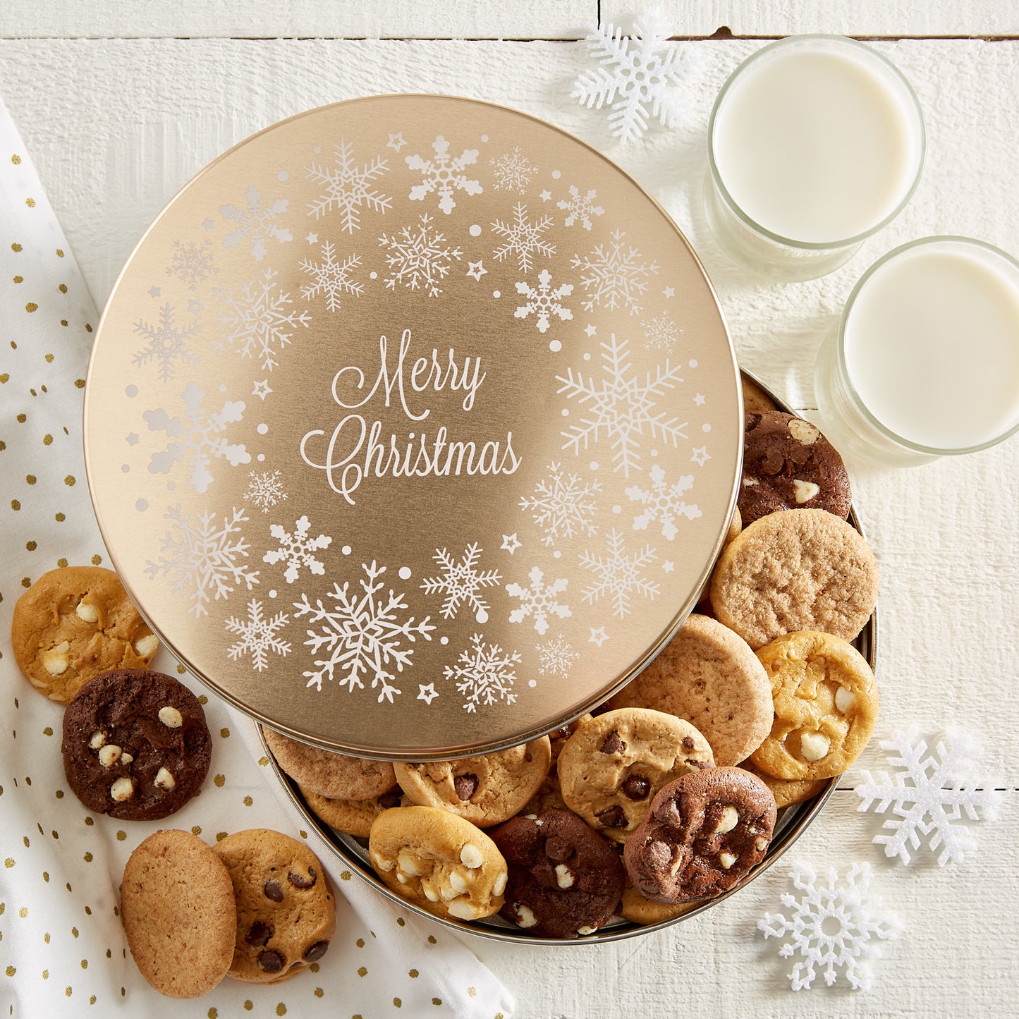 A gold round tin with a Merry Christmas sentiment covered in snowflakes and filled with Nibblers®