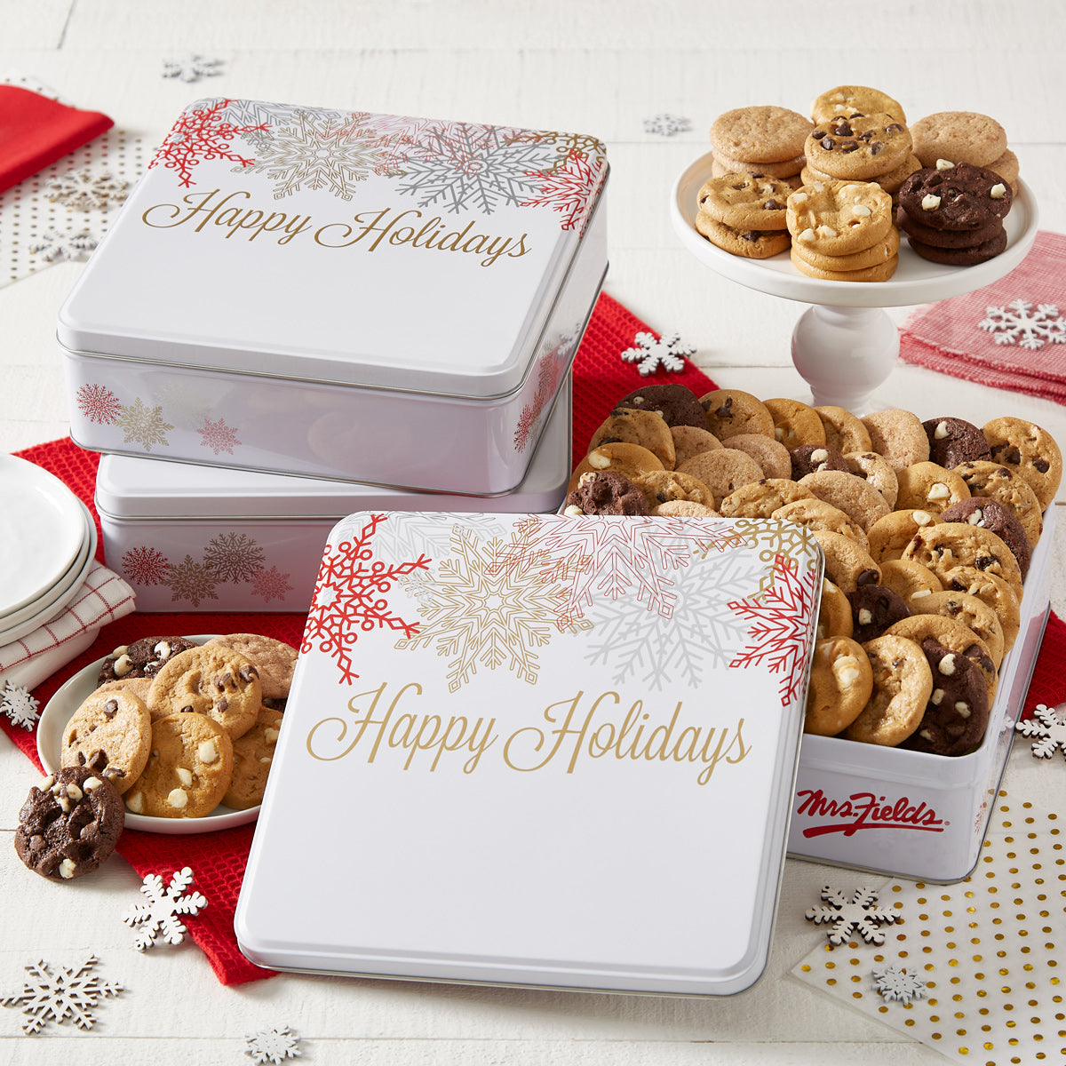Three Happy Holiday gift tins decorated with snowflakes and filled with Nibblers®