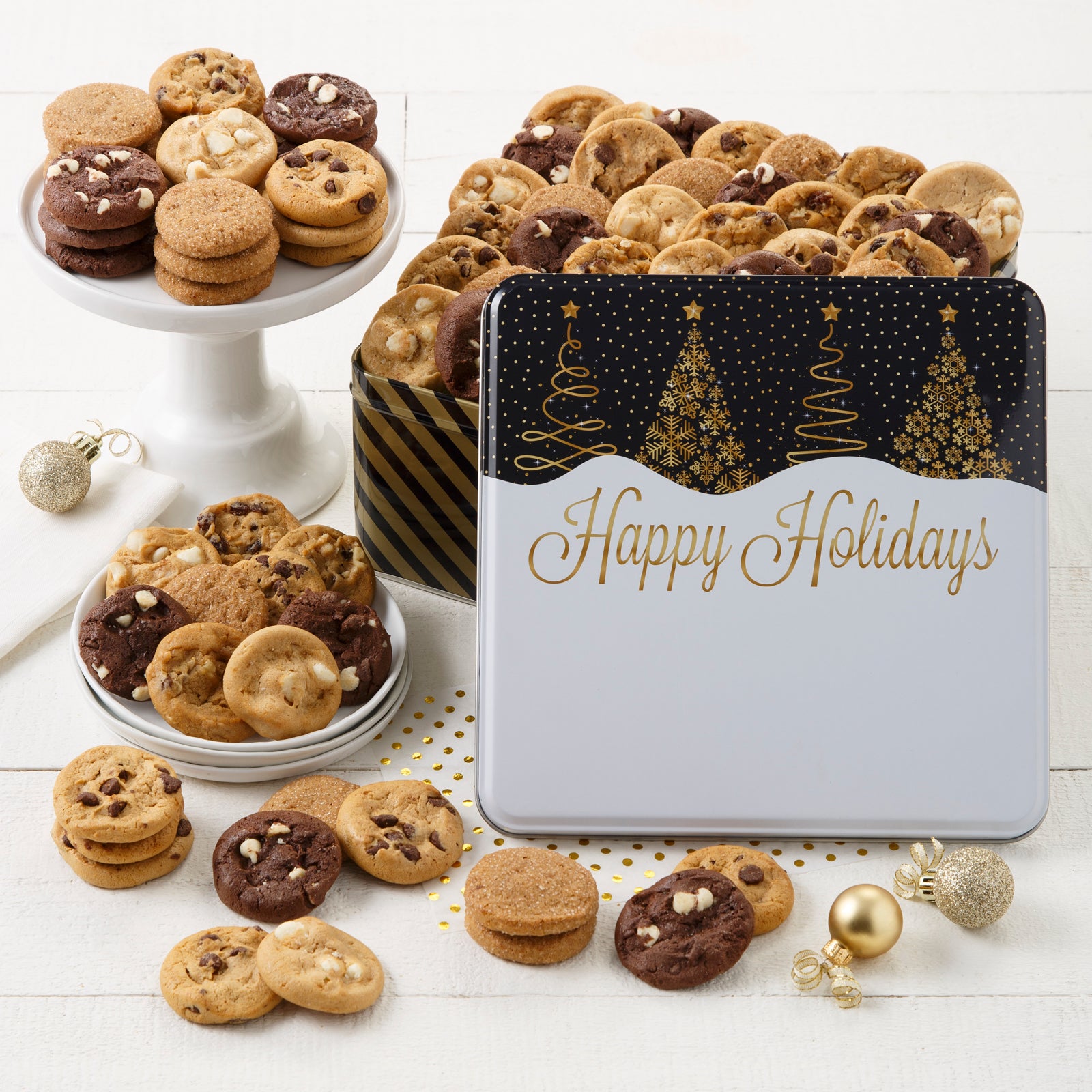 A happy holidays black and gold tin decorated with Christmas trees filled with an assortment of Nibblers®
