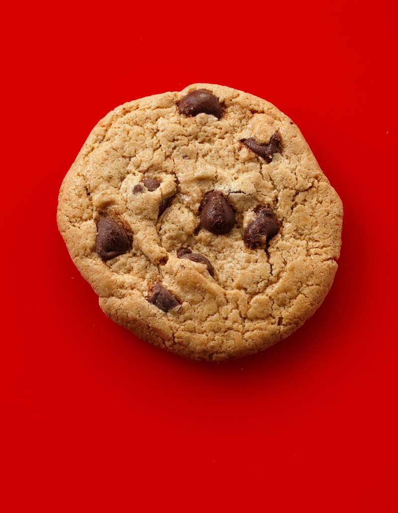 A single chocolate chip cookie photographed from above on a solid bright red background.