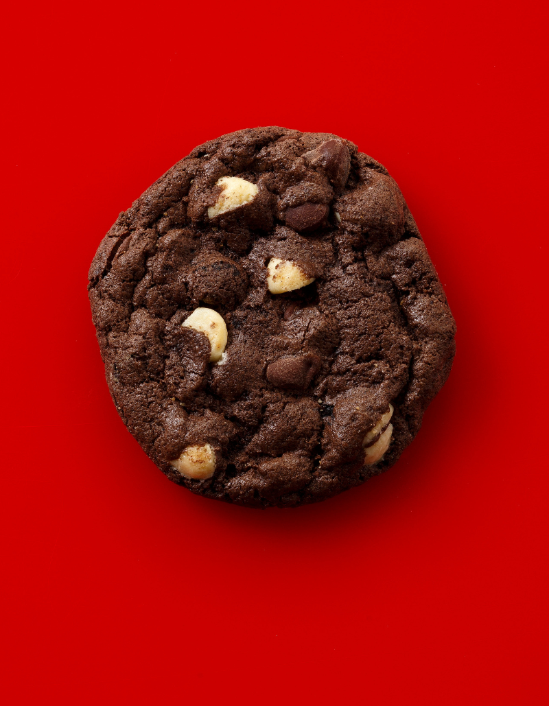 A chocolate cookie with white chocolate and semi-sweet chocolate chips in it on a red surface.