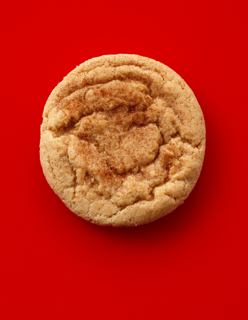 A single round cinnamon sugar cookie with a swirled cinnamon filling, photographed from directly above on a solid bright red background.