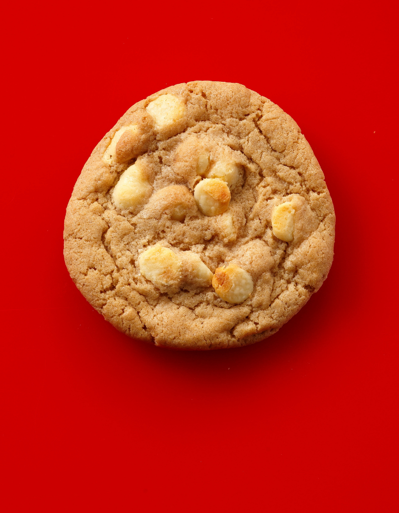 A single round chocolate chip cookie with white chocolate chips, photographed from directly above on a solid bright red background.