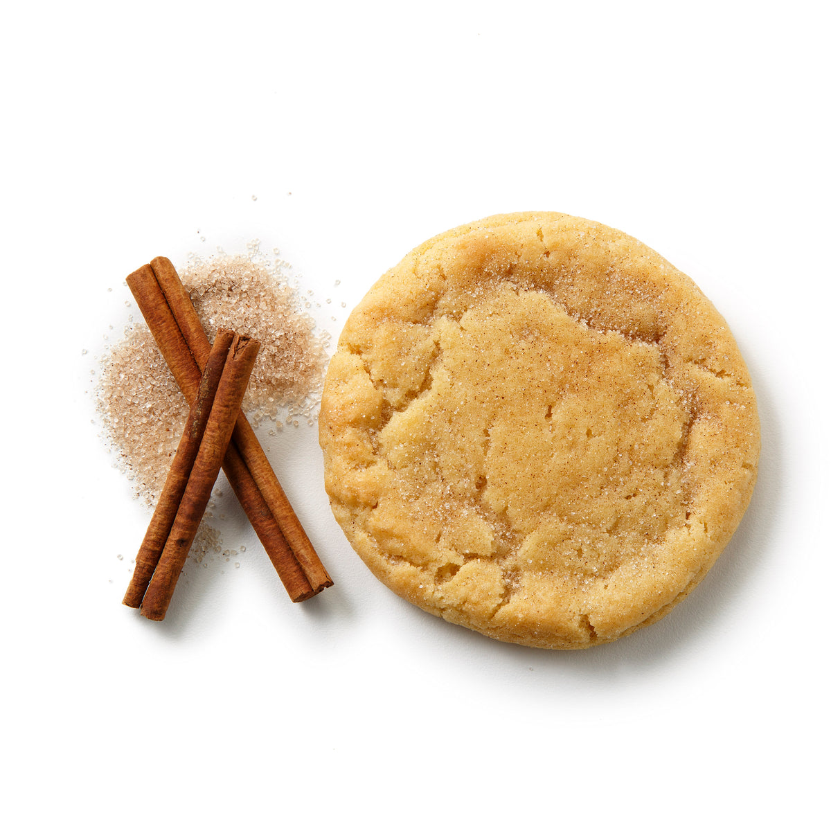 A round sugar cookie with cinnamon and sugar, shown next to two cinnamon sticks and a small pile of granulated sugar on a white background.
