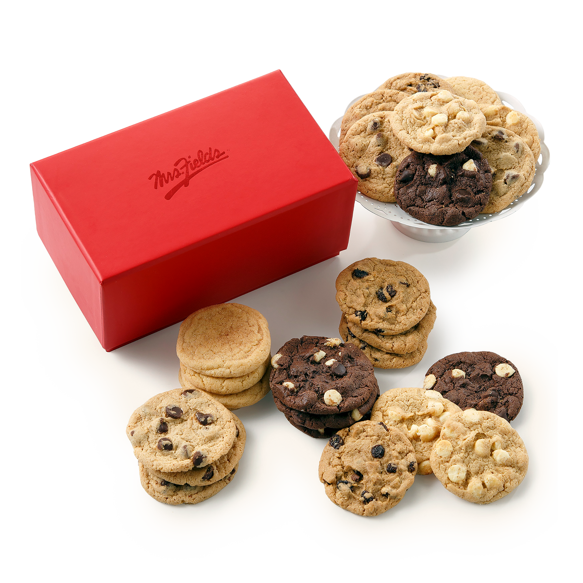 A red rectangular box with the brand name 'Mrs Fields' on the lid, arranged on a white background alongside assorted cookies including chocolate chip cookies, white chocolate chip cookies, and oatmeal cookies. A glass bowl filled with cookies sits behind the box.