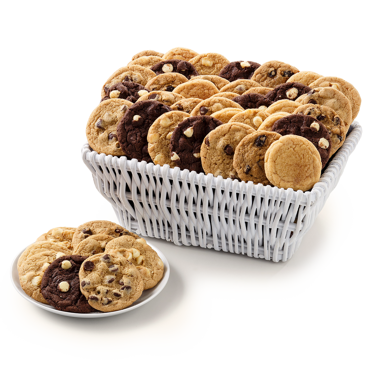 A white woven basket filled with assorted chocolate chip cookies, with a small plate of assorted cookies in the foreground on a clean white background.