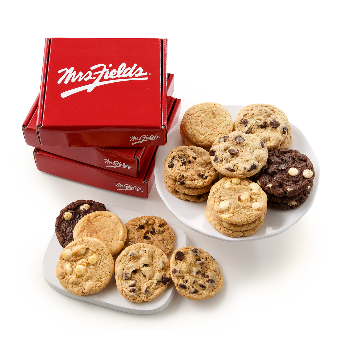 Three red Mrs. Fields cookie boxes stacked on a white background, with plates of assorted Mrs.