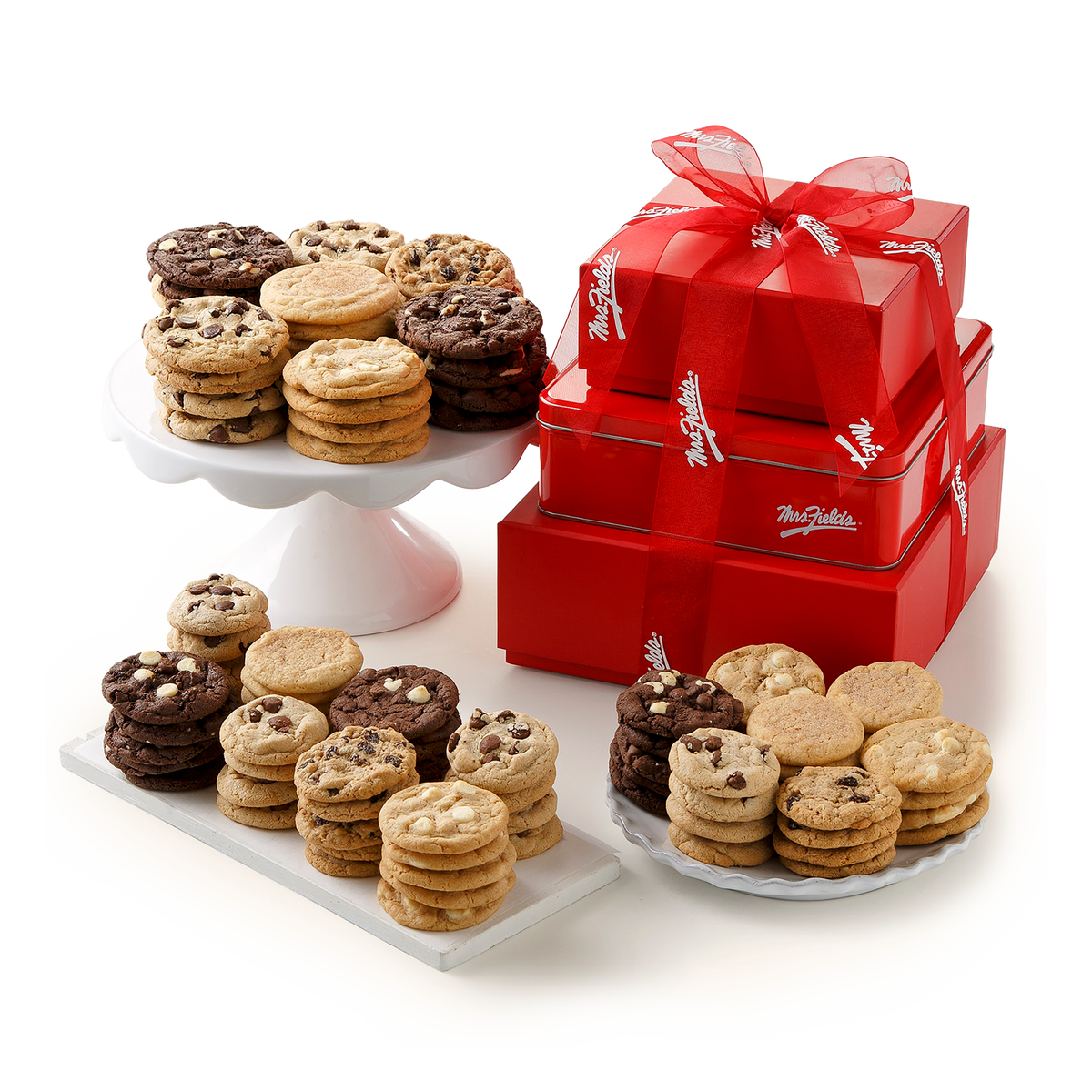 An assortment of chocolate chip and chocolate cookie bars arranged on white serving platters and a pedestal, alongside three stacked red gift boxes with red ribbons and white script branding, photographed on a clean white background.