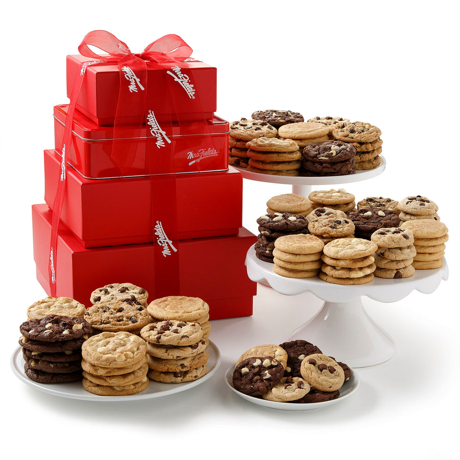 A large four-tier tower composed of red gift boxes and tied with a red Mrs. Fields ribbon surrounded by a large assortment of big and small cookies on a blank white surface.