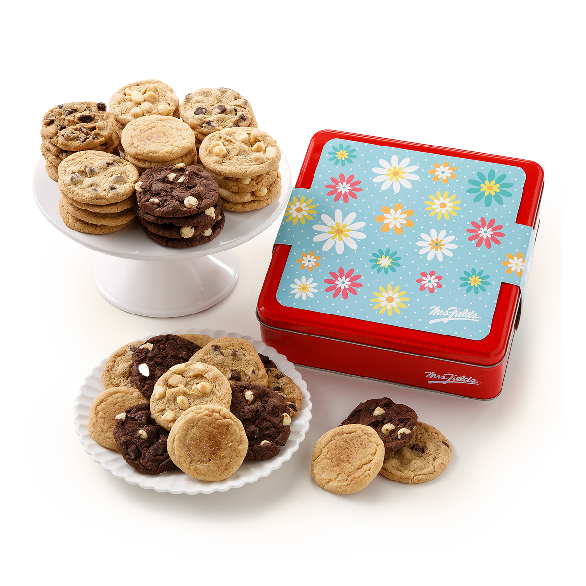 A red metal cookie tin with a blue floral lid and a white ribbon, filled with assorted cookies, displayed on a white background with some cookies on plates.
