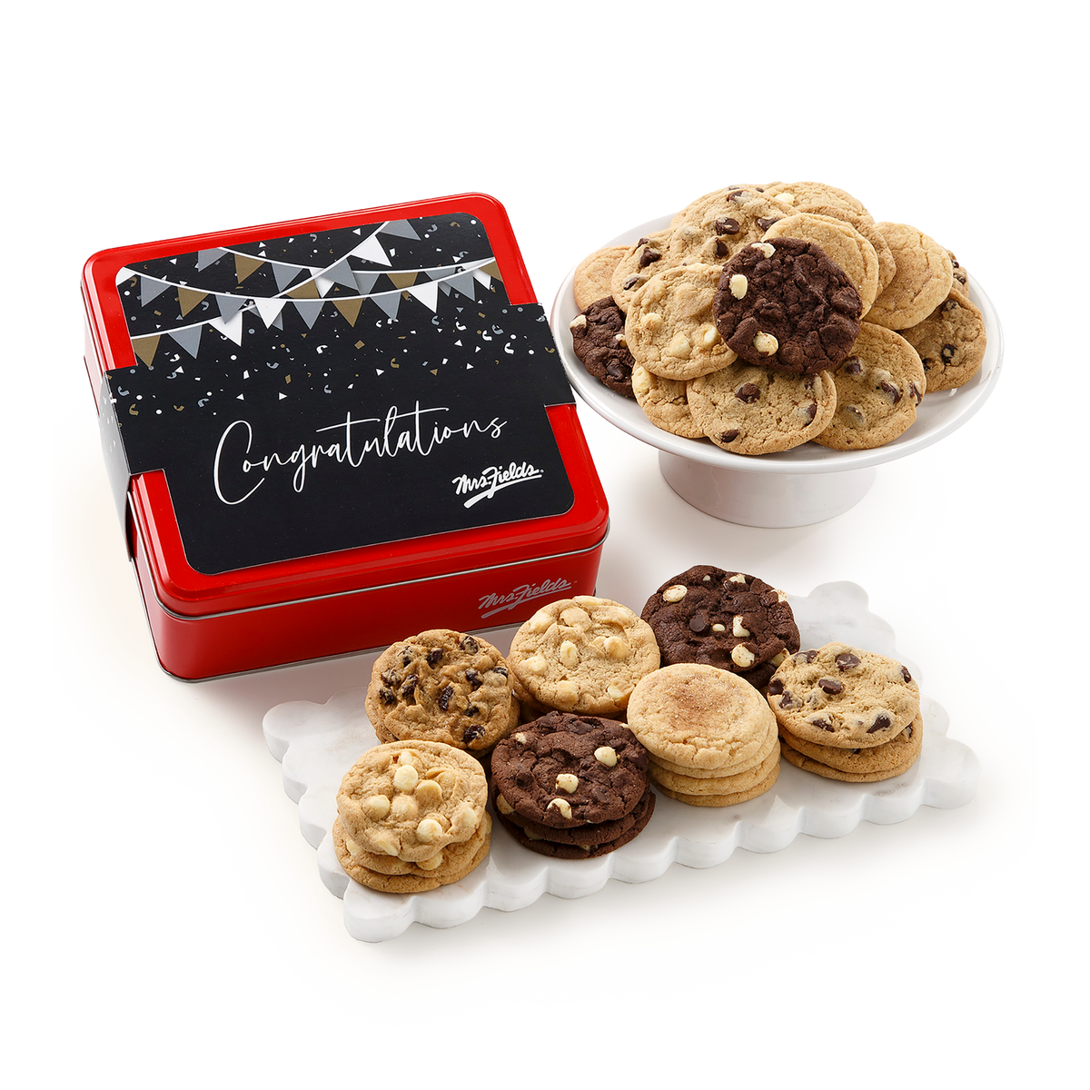 A red and black gift tin with a 'Congratulations' banner, styled with assorted chocolate chip cookies on white ceramic platters against a clean white background.