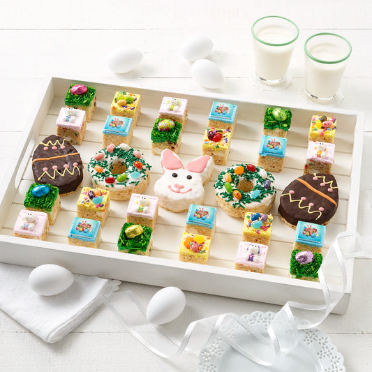 Twenty four mini square rice krispie treats and five large rice krispie treats (two easter eggs, two easter wreaths with jelly beans, and one bunny  shaped treat) all decorated in an Easter and spring theme topped with chocolate, candies, and bunnies.