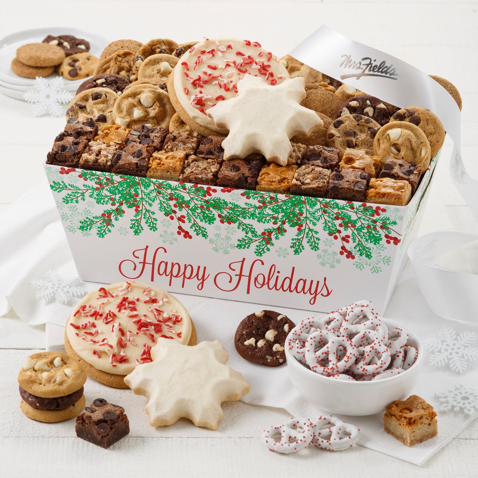 A Happy Holidays with holly decorations crate with an assortment of Nibblers®, brownie bites, two frosted peppermint round cookies with sprinkles, two frosted snowflakes and yogurt-covered pretzels