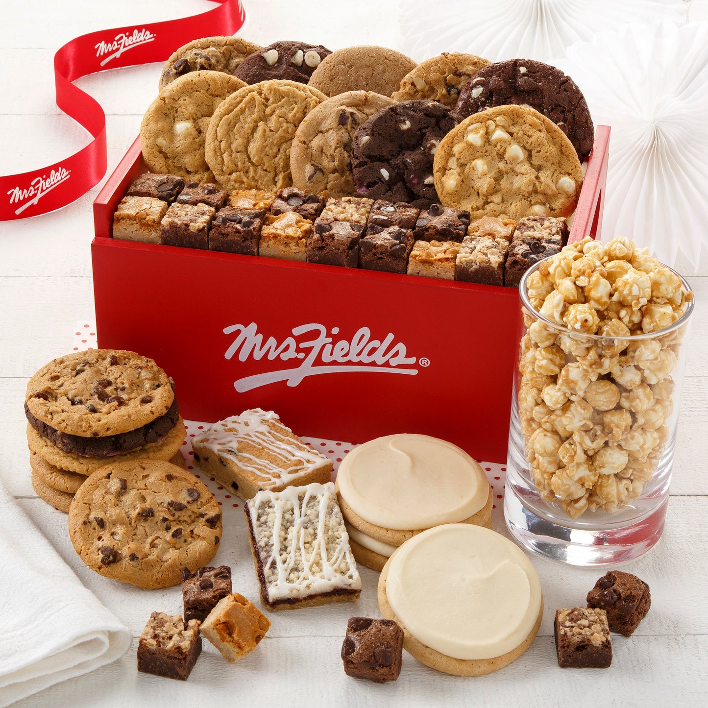 A red signature Mrs. Fields wooden crate filled with an assortment of original cookies, brownie bites, fruit bars, and popcorn