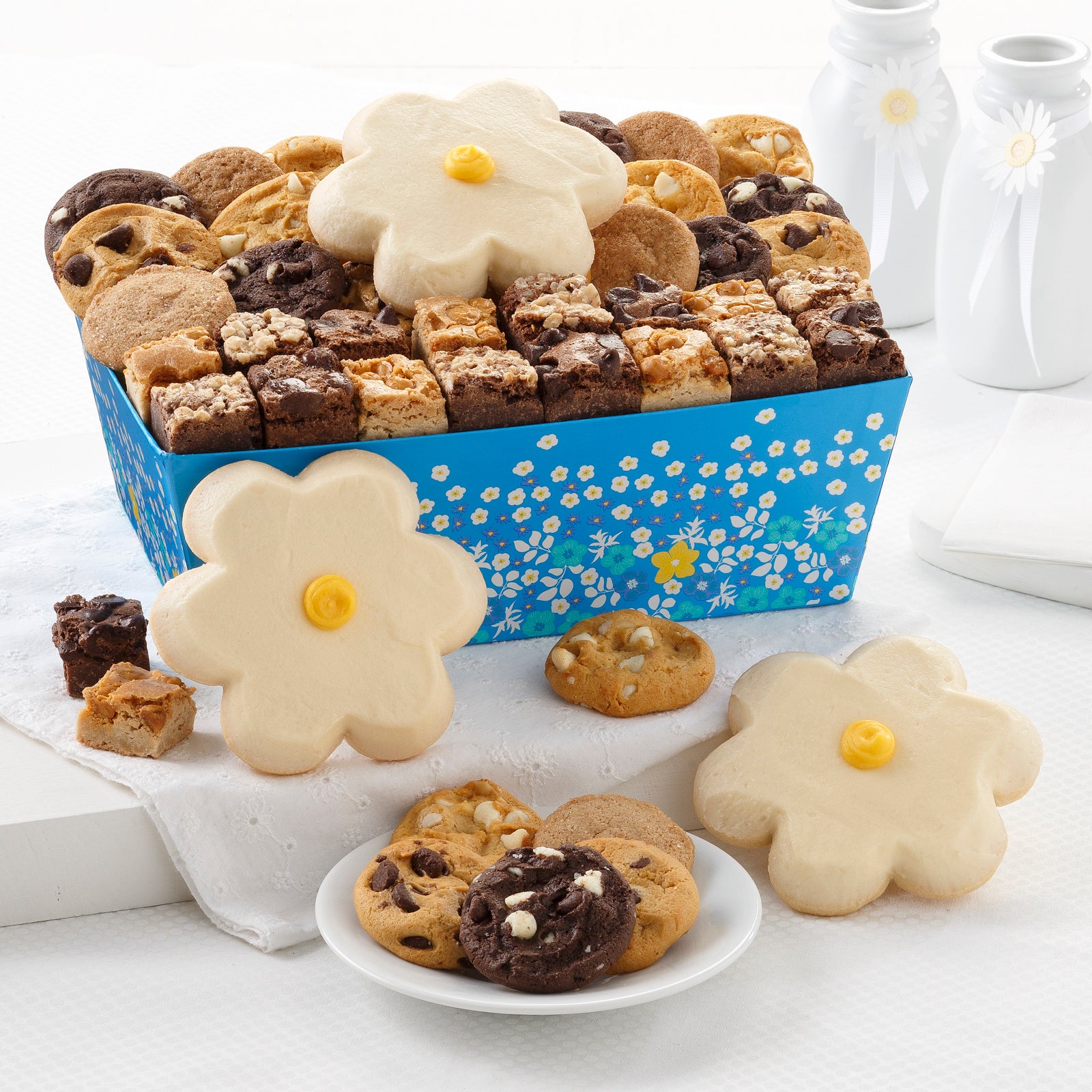 A blue floral gift crate filled with an assortment of nibblers, brownie bites, and frosted daisy cookies