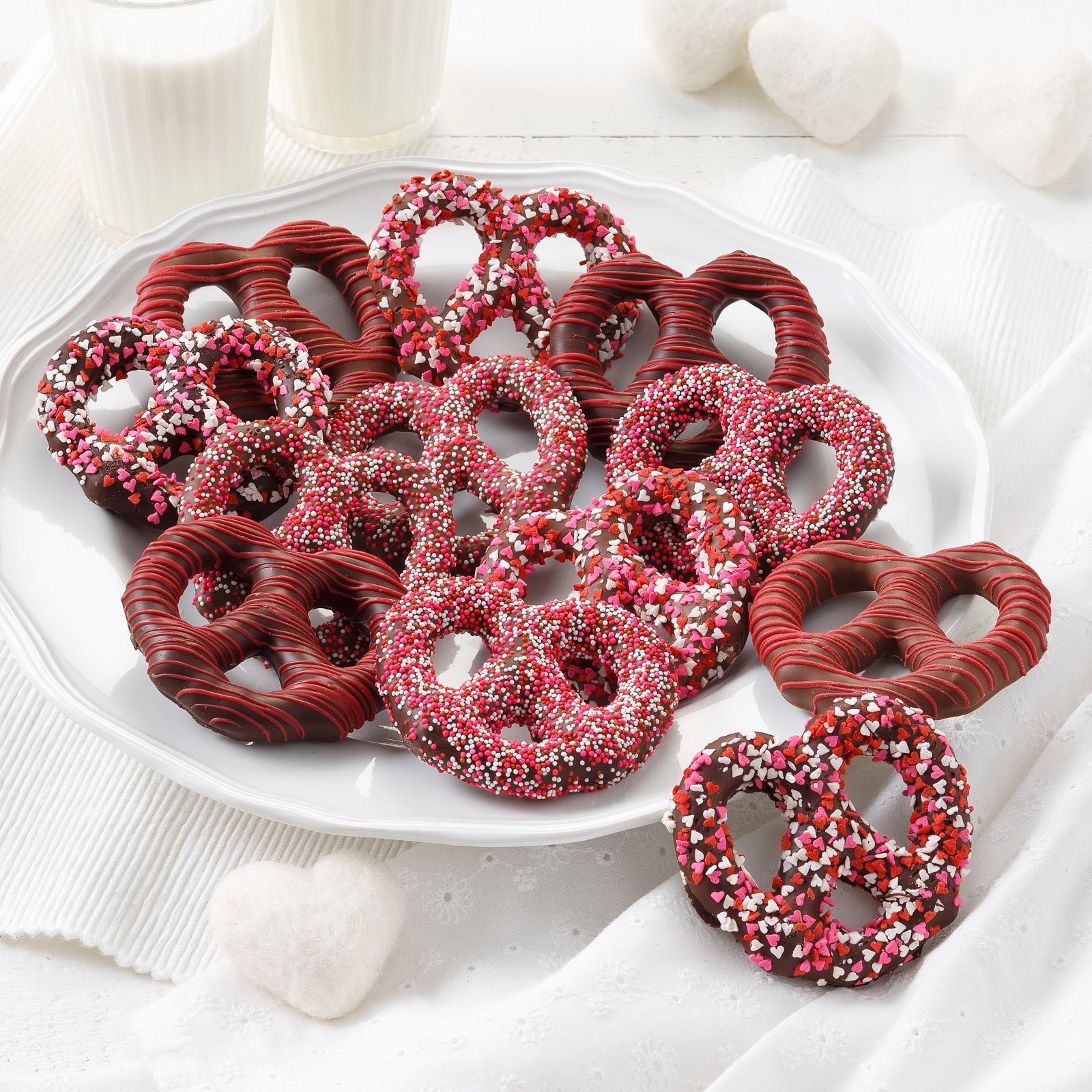 A dozen red and white Valentine's Day themed chocolate covered pretzels that are covered in sprinkles