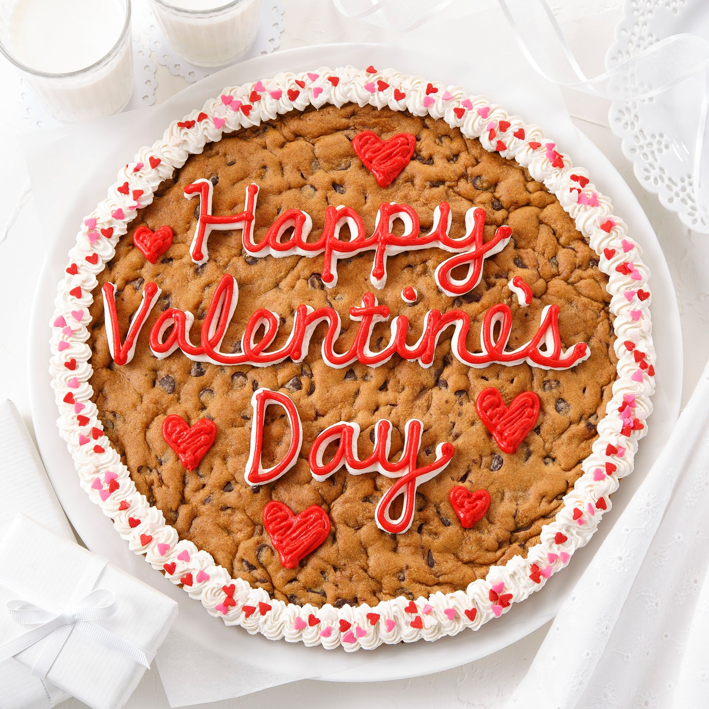 A Happy Valentine's Day cookie cake decorated with red and white frosting and heart-shaped sprinkles.
